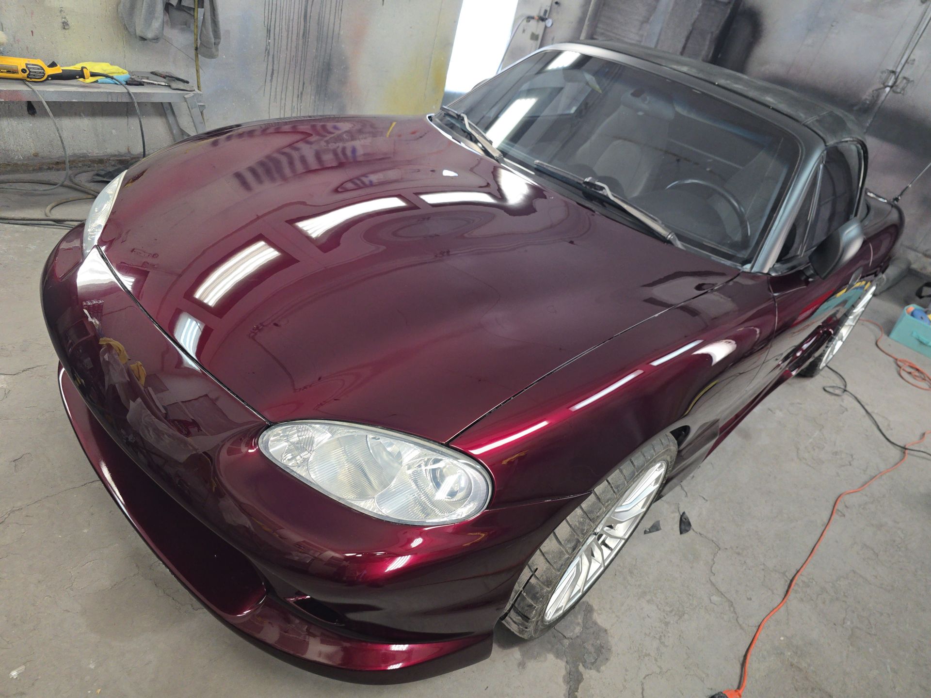 Maroon sports car in a garage, angled front view with shiny paint and silver wheels
