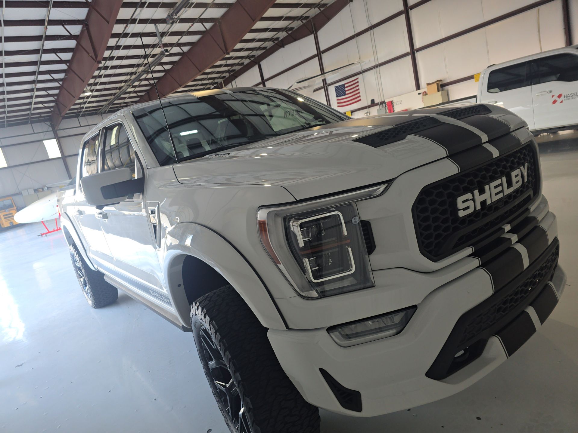 White Shelby pickup truck with black racing stripes parked inside a warehouse-like garage