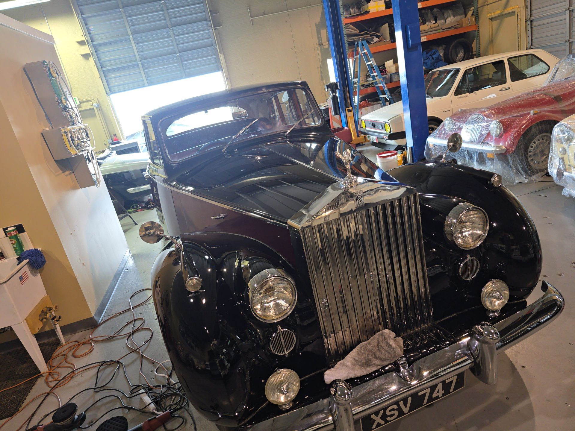 Classic black Rolls-Royce in a garage, front view with chrome grille and round headlights.