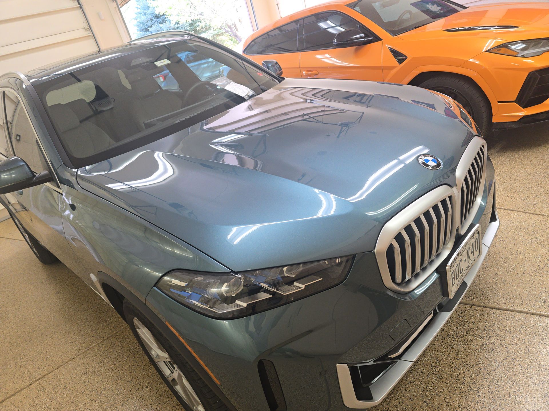 Blue-gray BMW SUV parked indoors beside an orange sports car