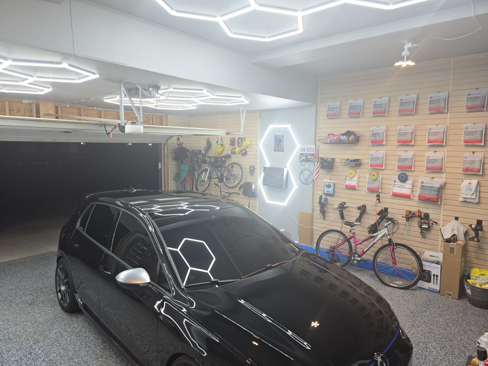 Black car in a modern garage with hexagon lights, wall decor, and bicycles.