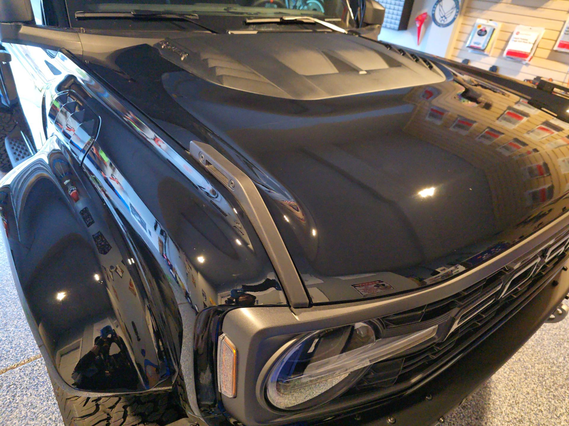 Black classic car with chrome details and blue headlights displayed indoors in a showroom.