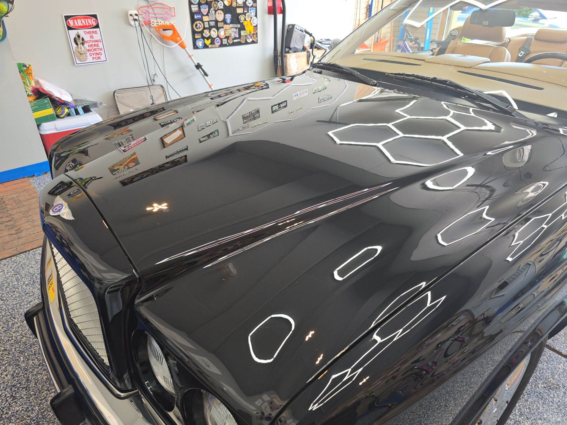 Glossy black car hood in an indoor garage, reflecting ceiling lights and wall posters