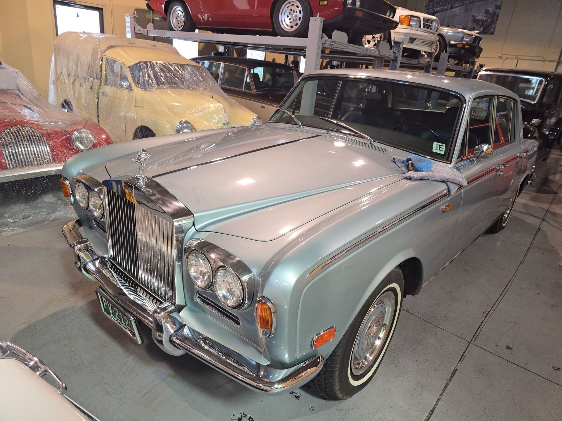 Classic silver Rolls-Royce sedan in a garage, with cars covered in the background.