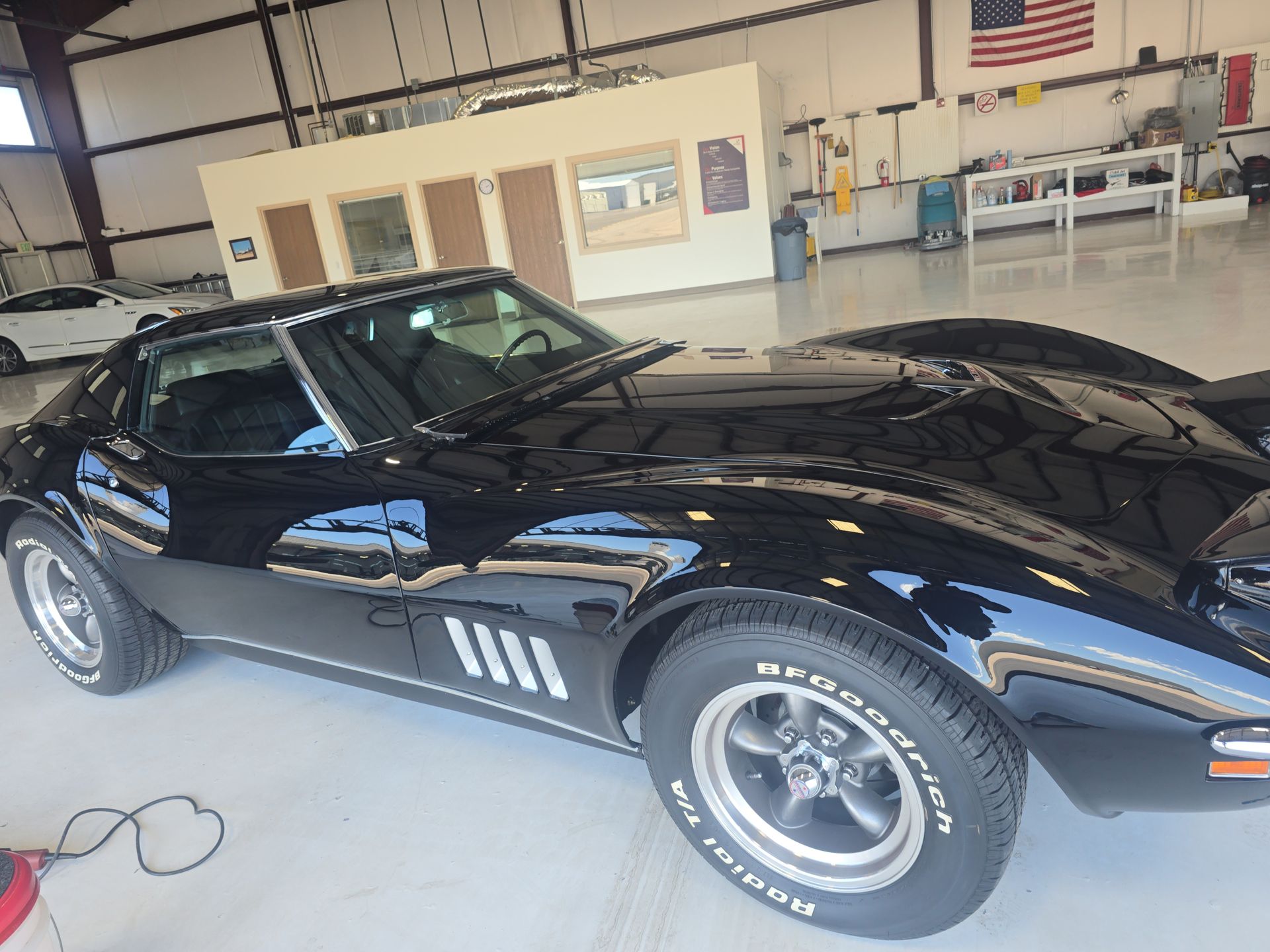 Black sports car parked in a garage, side view with glossy finish and racing stripes