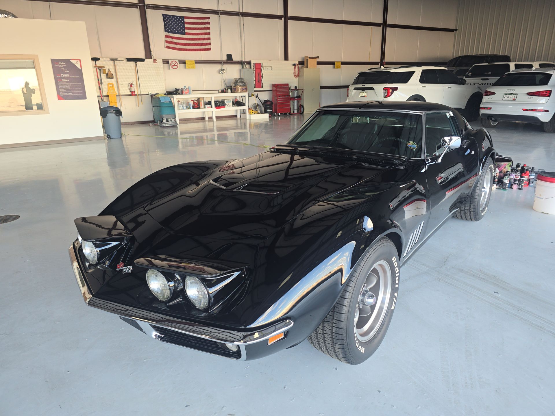 Black classic sports car in a garage with an American flag on the wall