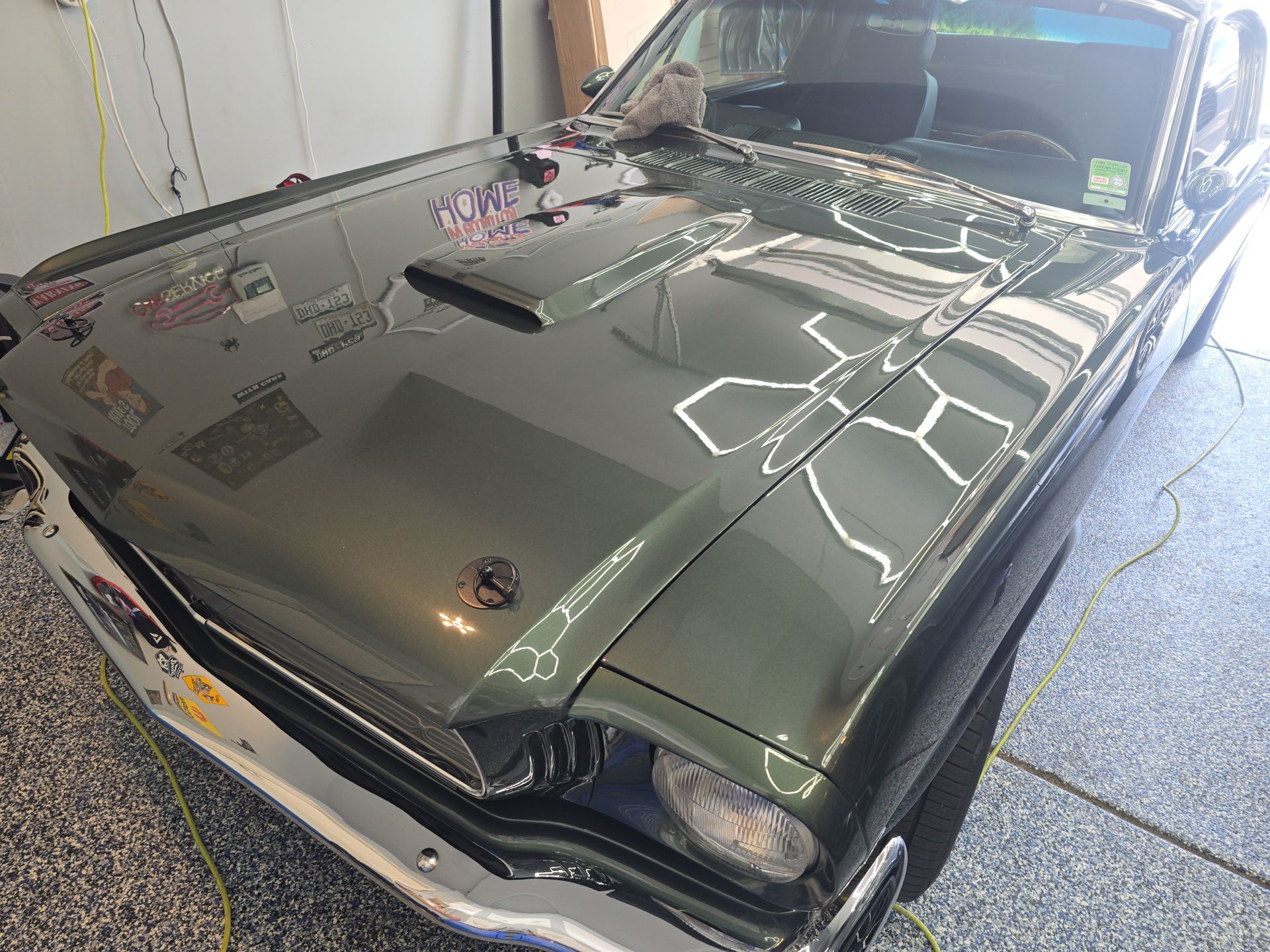 Classic dark green car with hood scoop parked in a garage, viewed from the front-left side