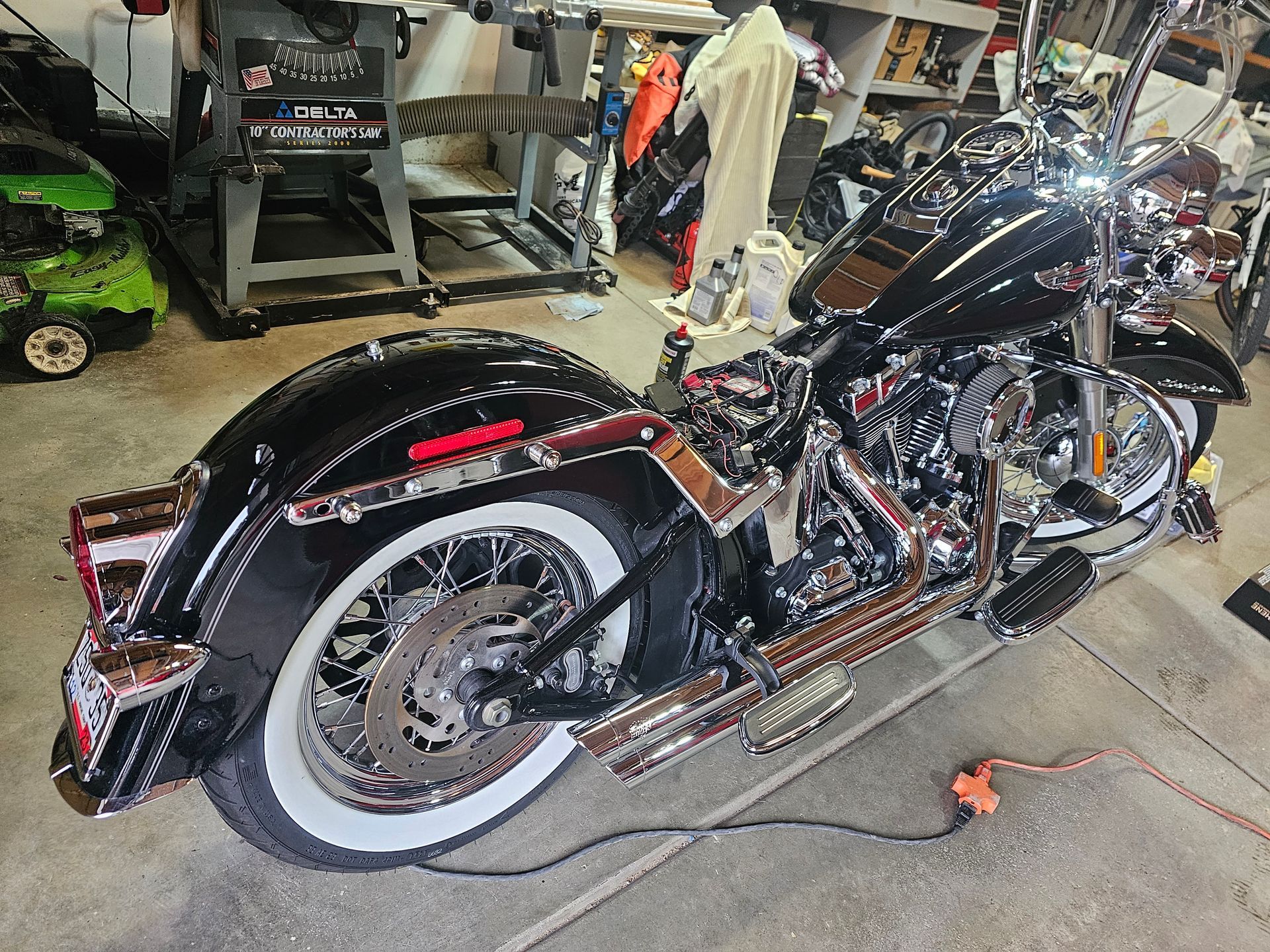 Custom black-and-chrome motorcycle with whitewall tires in a garage, viewed from the rear side.