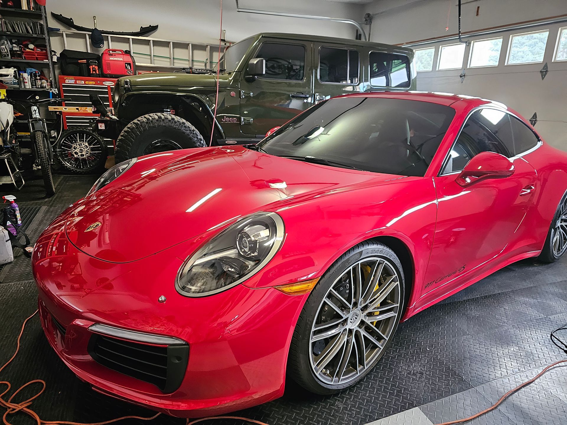 Red sports car in a garage, with off-road vehicles and shop equipment in the background