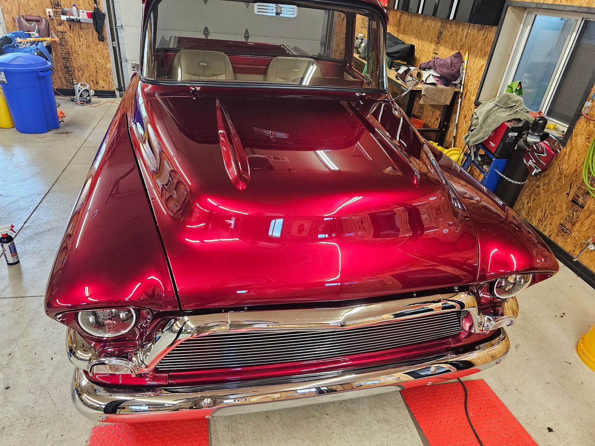 Red classic car with glossy maroon paint parked in a garage, rear view