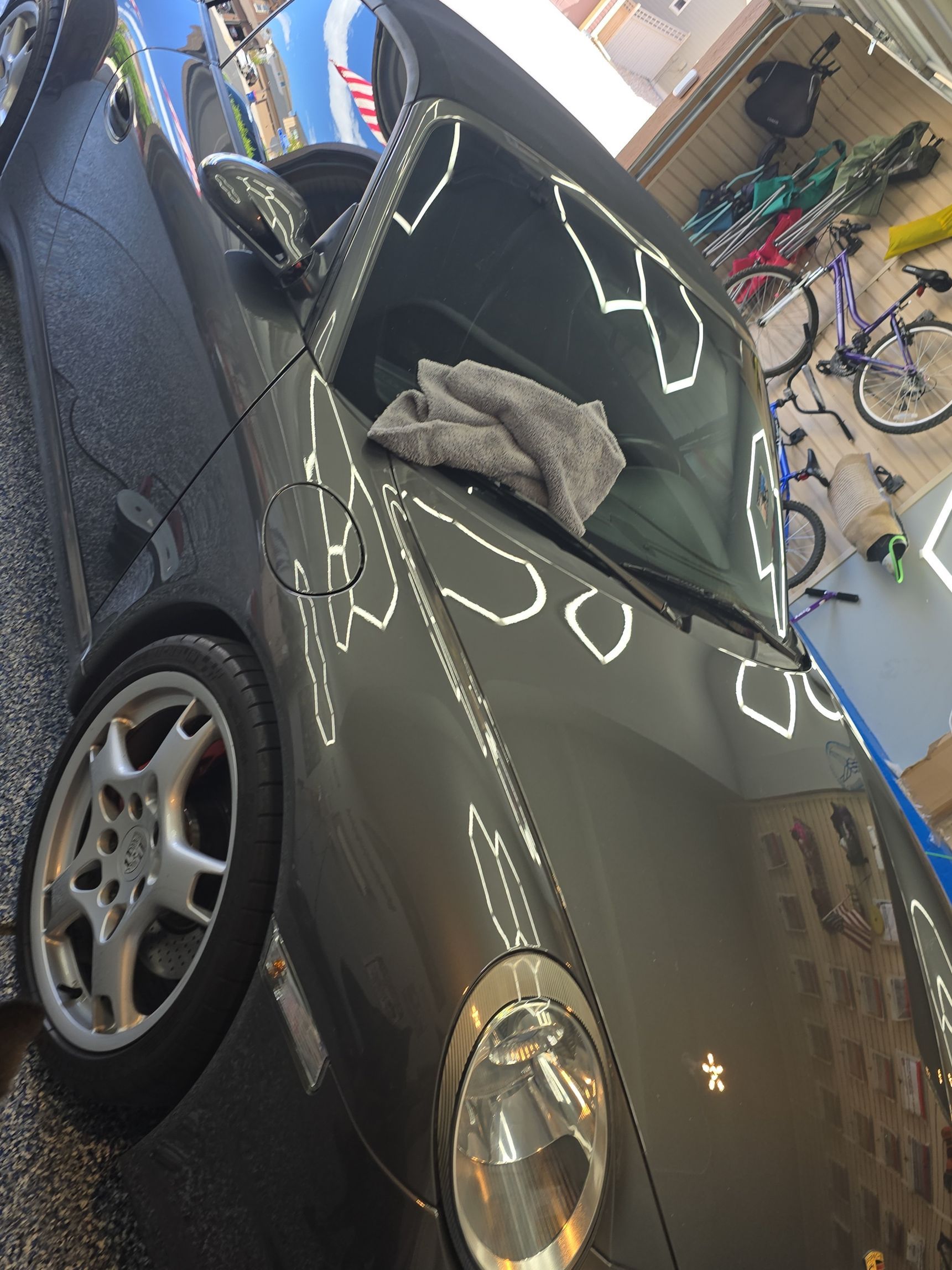 Black sports car in a garage with windshield damage and a gray cloth on the hood
