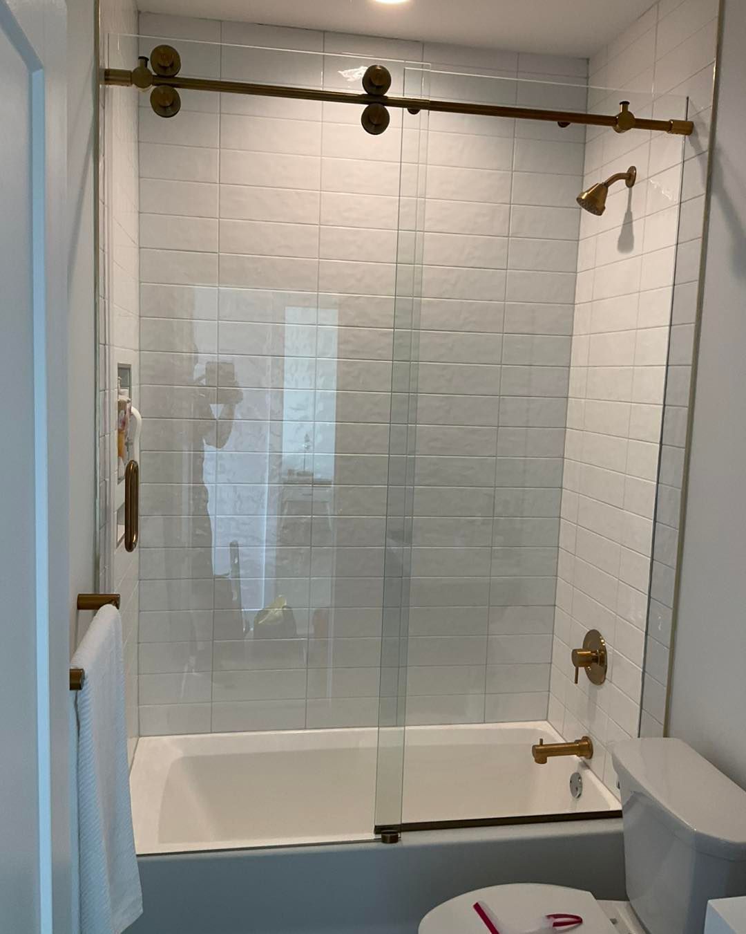 Bathroom with white subway tile, glass shower door, brass fixtures.