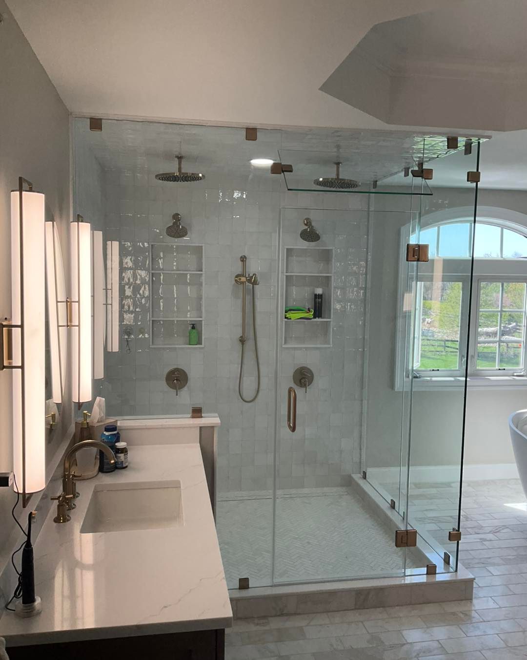 A modern bathroom with a glass shower, dual shower heads, and a white vanity with gold fixtures.