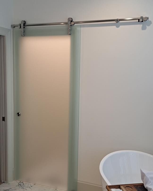 Frosted glass sliding door, silver hardware on white wall, bathroom setting.