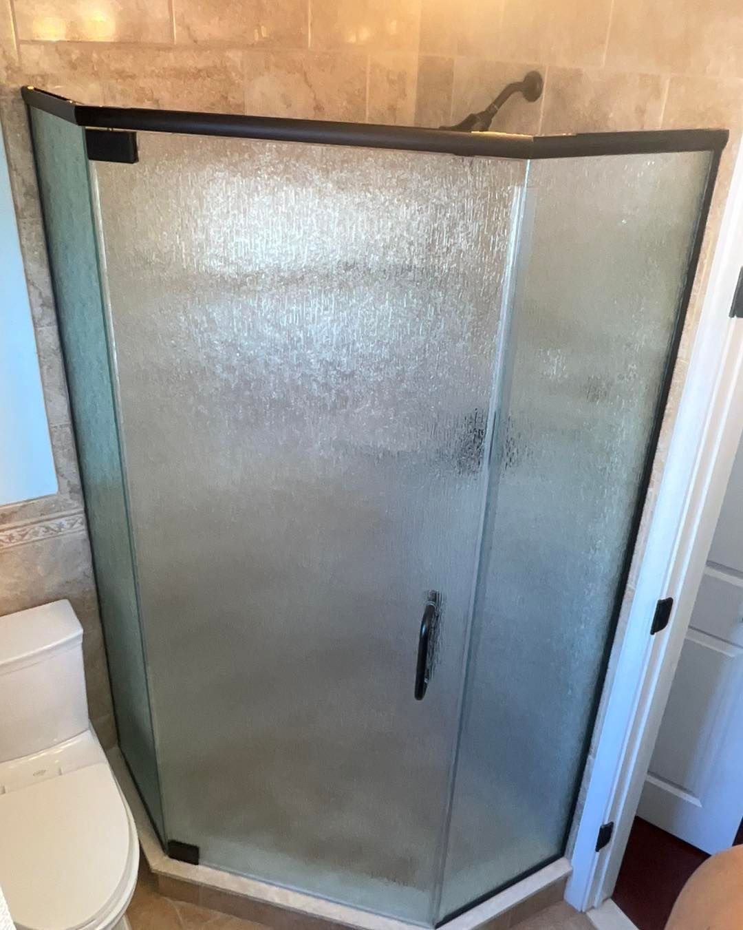 Corner shower with frosted glass door, black frame, and a handle.