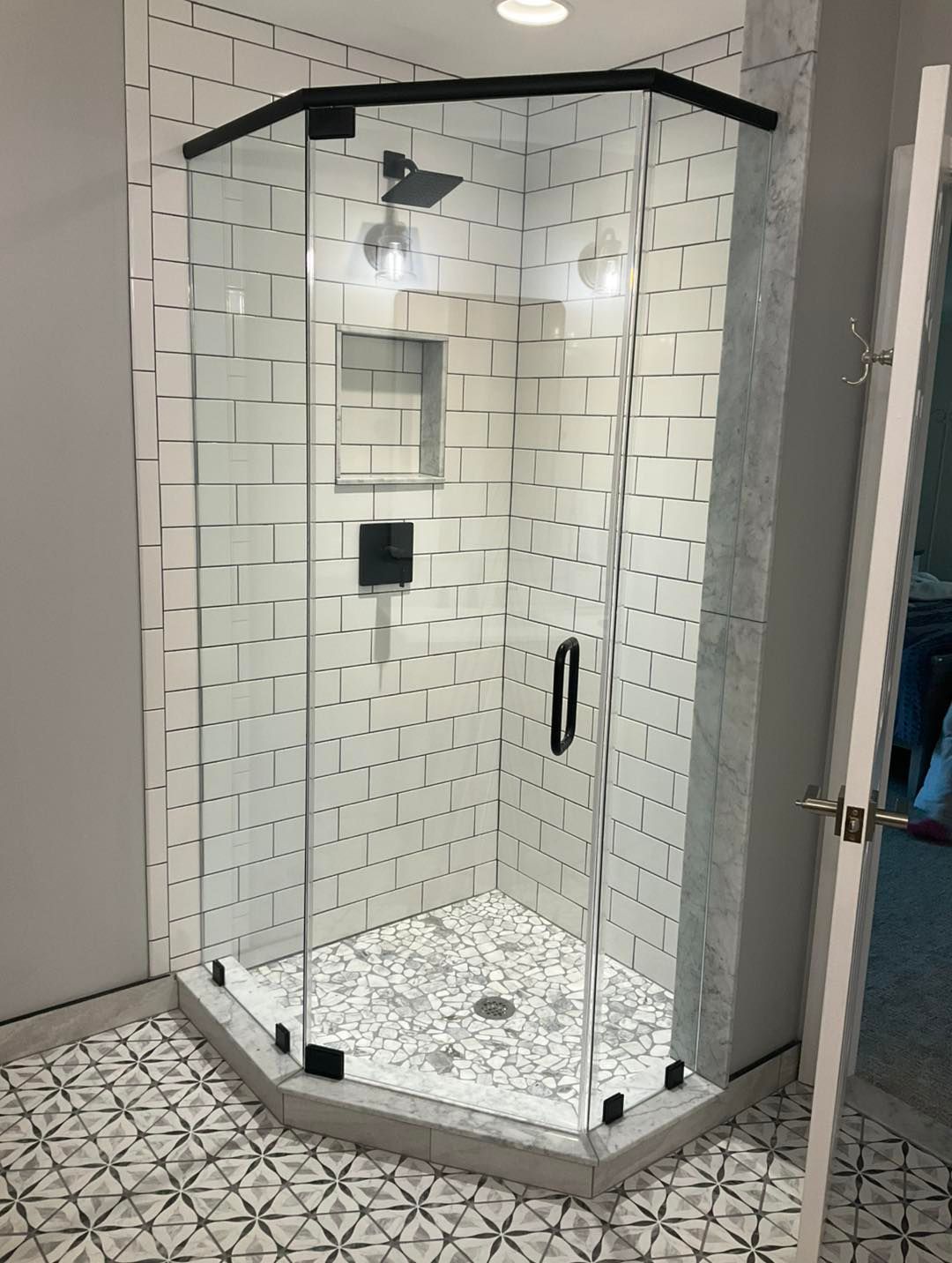 A modern, clear glass shower enclosure with black trim in a tiled bathroom.