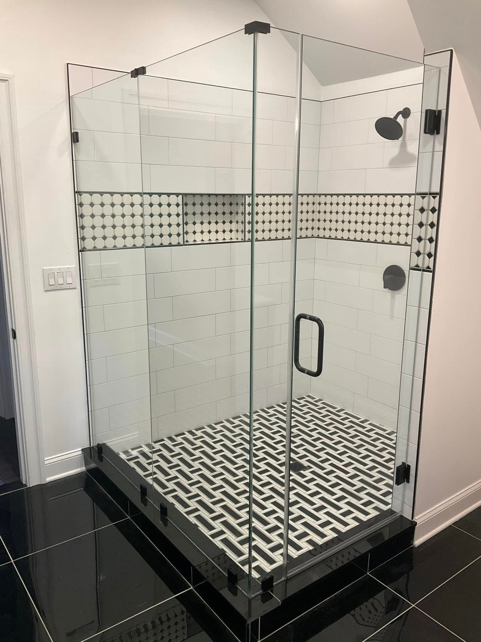 Glass shower enclosure with black and white tile floor and accents.