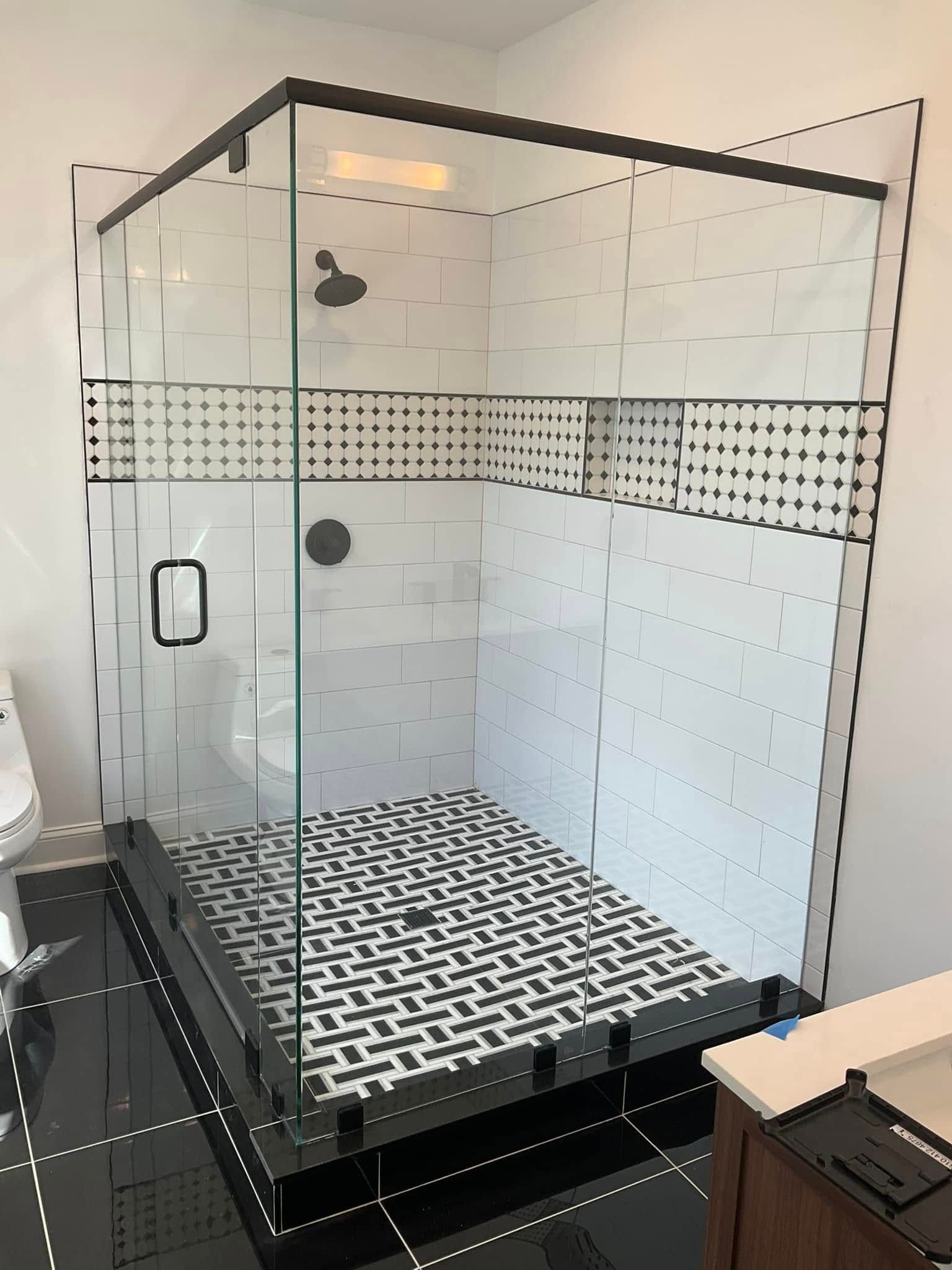 Modern glass shower with black accents and patterned tile floor. White tiled walls.