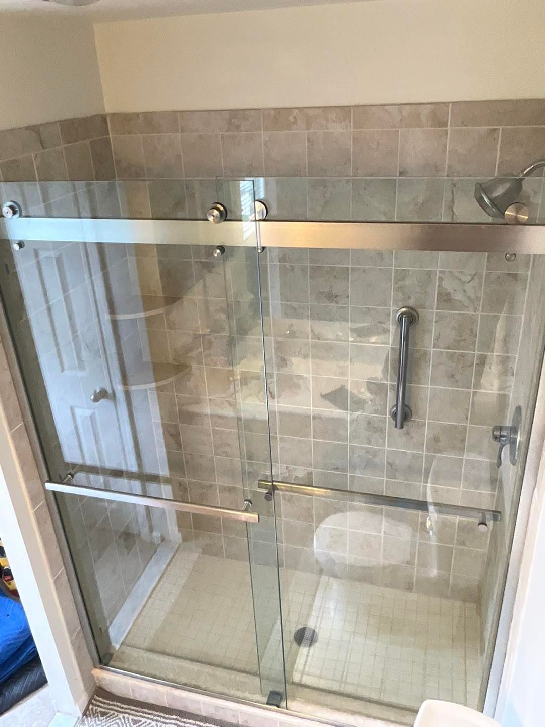 A glass shower enclosure with sliding doors and a chrome grab bar on a tiled wall.
