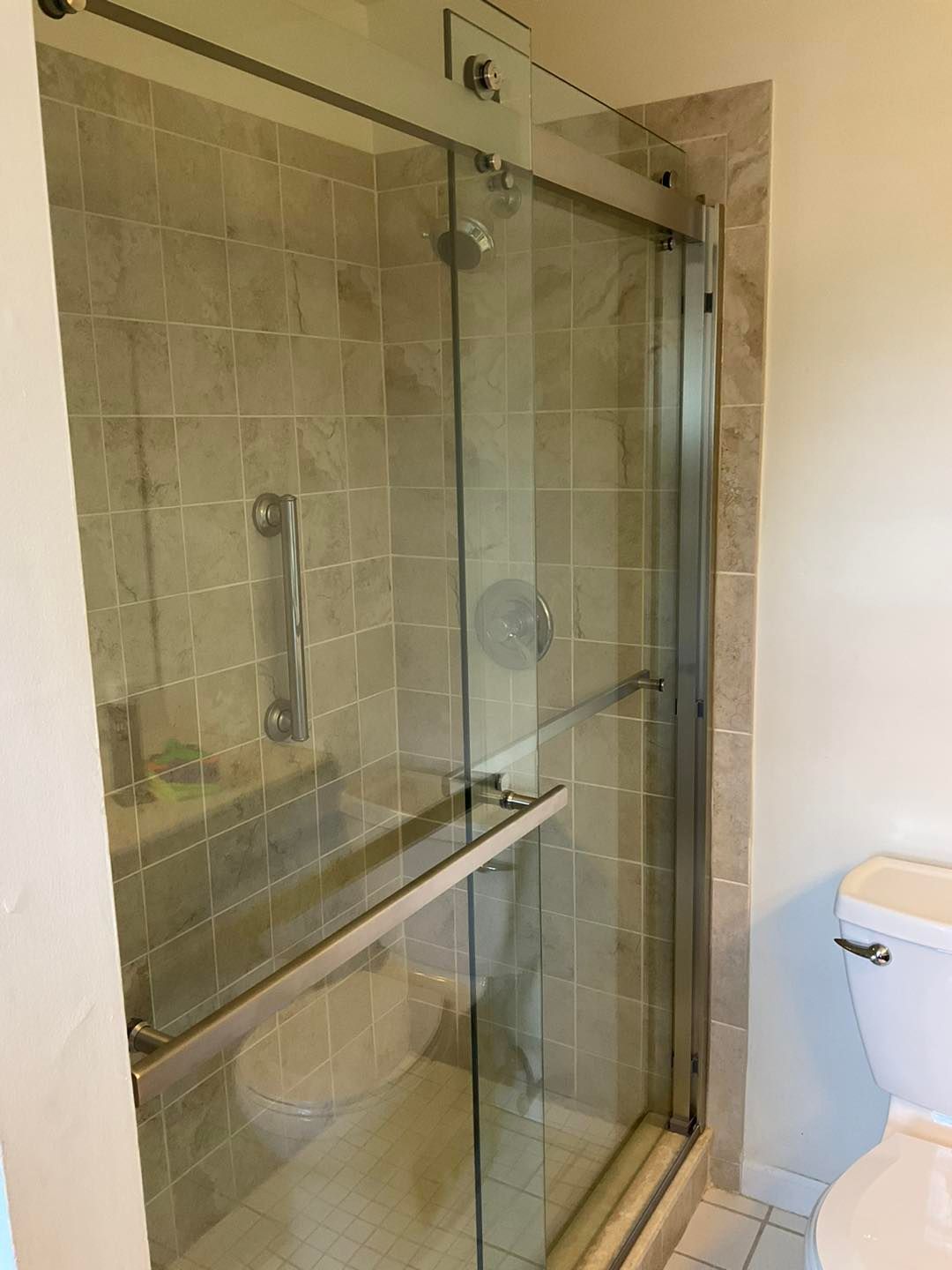 Shower stall with glass doors, silver frame, and tile walls. A toilet sits to the right.