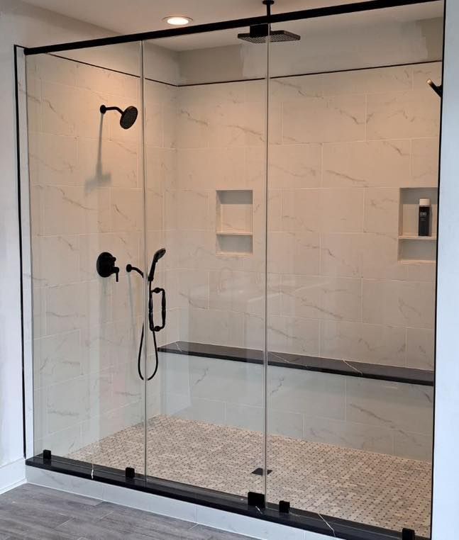 Modern shower with black fixtures and glass doors; white tiled walls; mosaic floor.