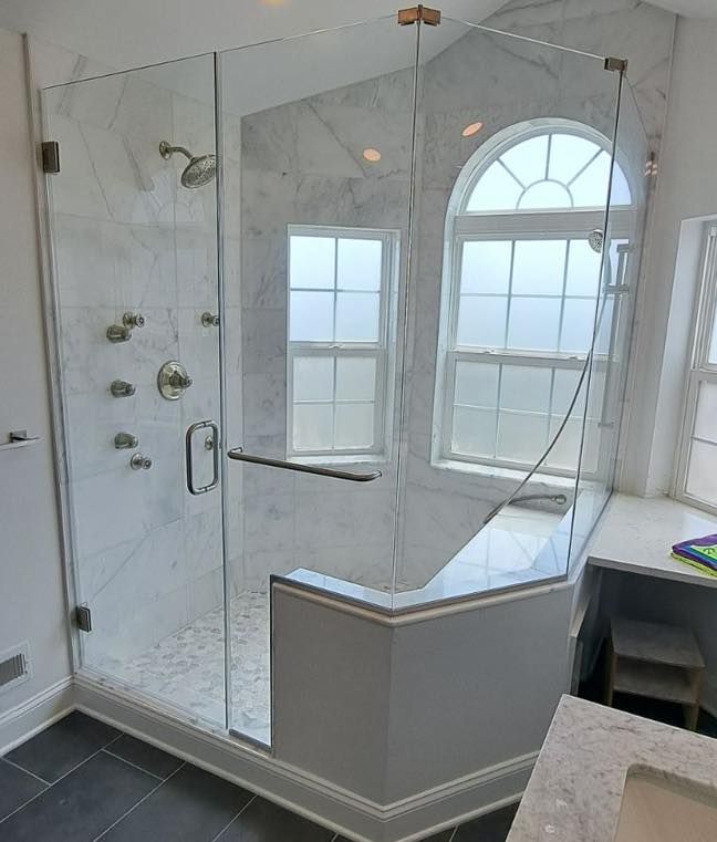 Glass shower enclosure with marble tile walls and two windows.