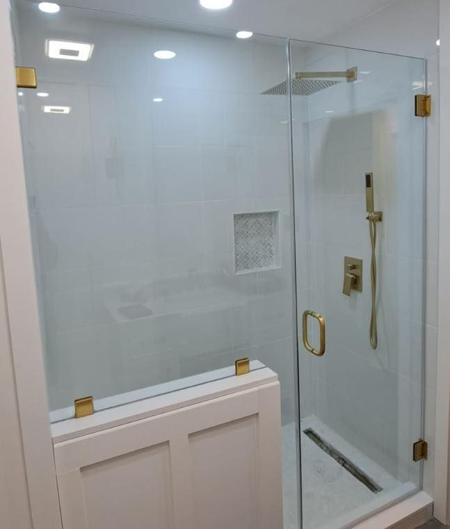 Modern bathroom with a glass shower enclosure, gold hardware, and white tile.