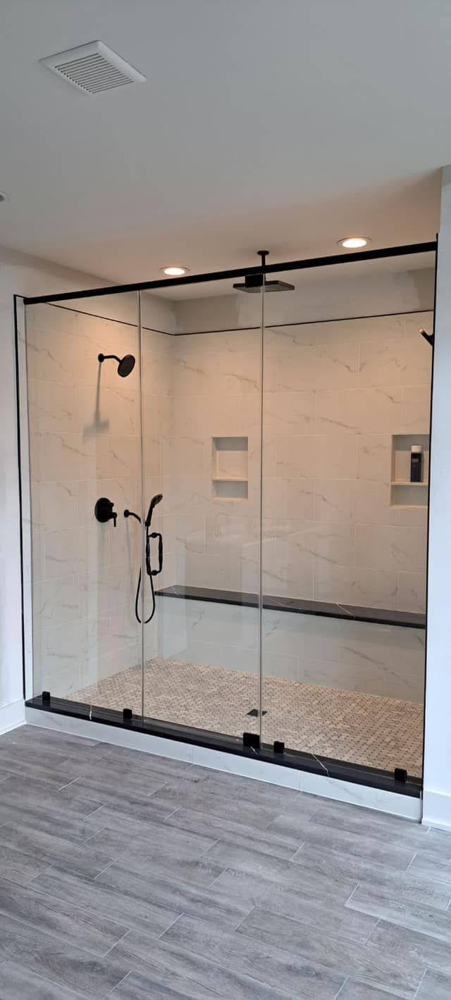 A modern, glass-enclosed shower with pebble flooring and black fixtures, set against light-colored tile walls.