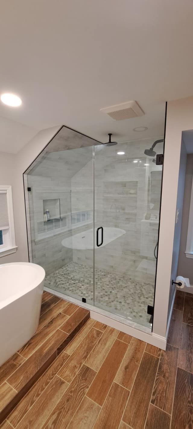Modern bathroom with glass shower, freestanding tub, and wood-look tile.