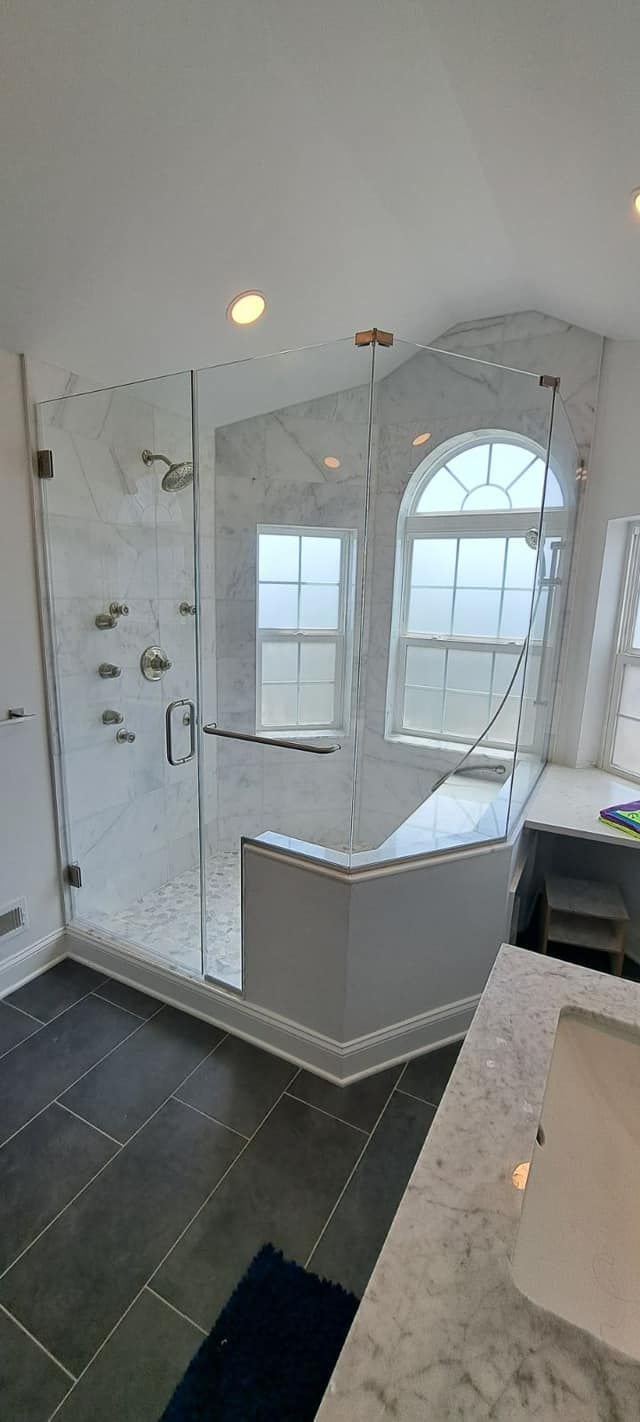 A luxurious bathroom with a large glass shower, a window, and dark tile flooring.