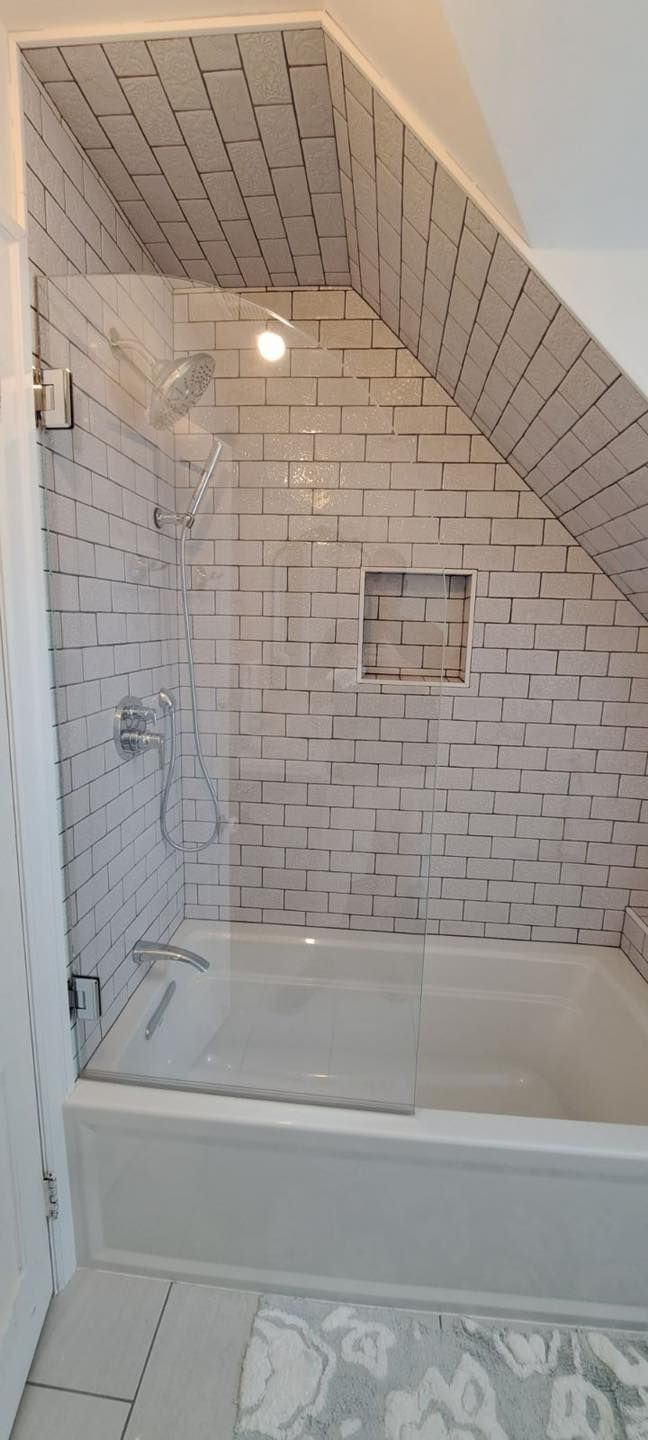 Bathroom with white brick-patterned tiles, a tub, and a clear glass shower screen under a sloped ceiling.