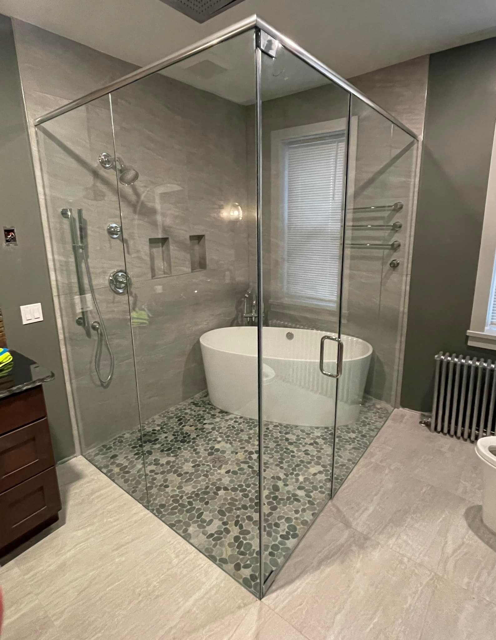 Modern bathroom with glass shower, tub, and stone floor. Gray and white color scheme.