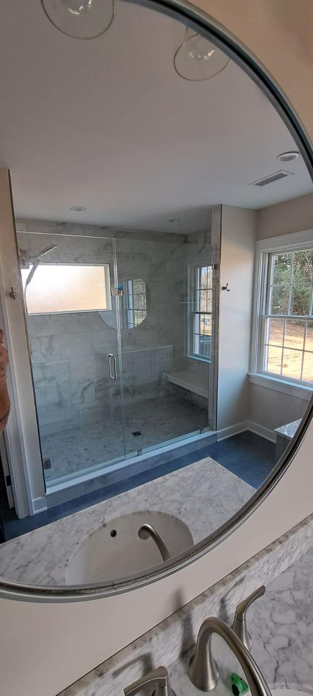 Bathroom mirror reflects a shower with glass doors, a built-in bench, and a sink on a marble countertop.