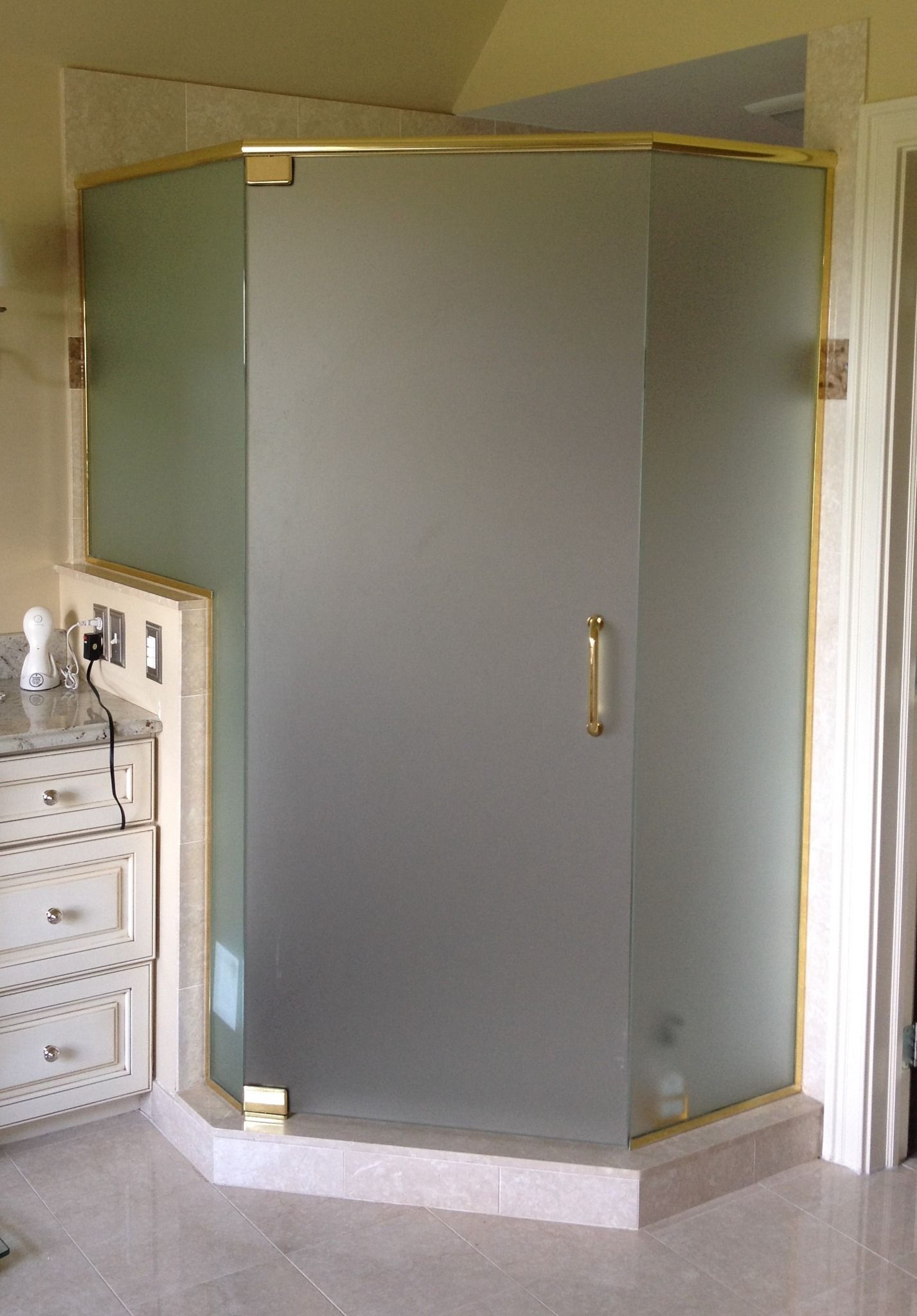 Corner shower with frosted glass doors and gold hardware.