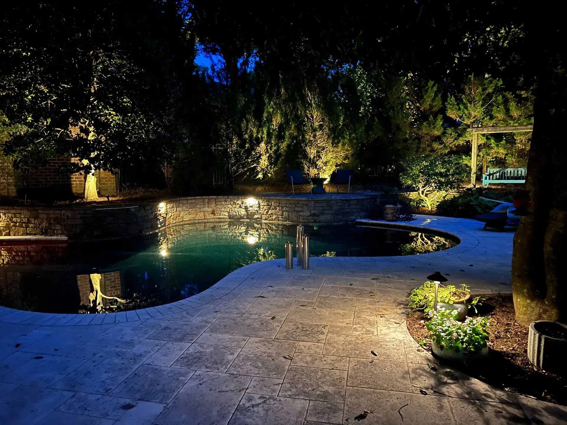 A swimming pool is lit up at night in a backyard.