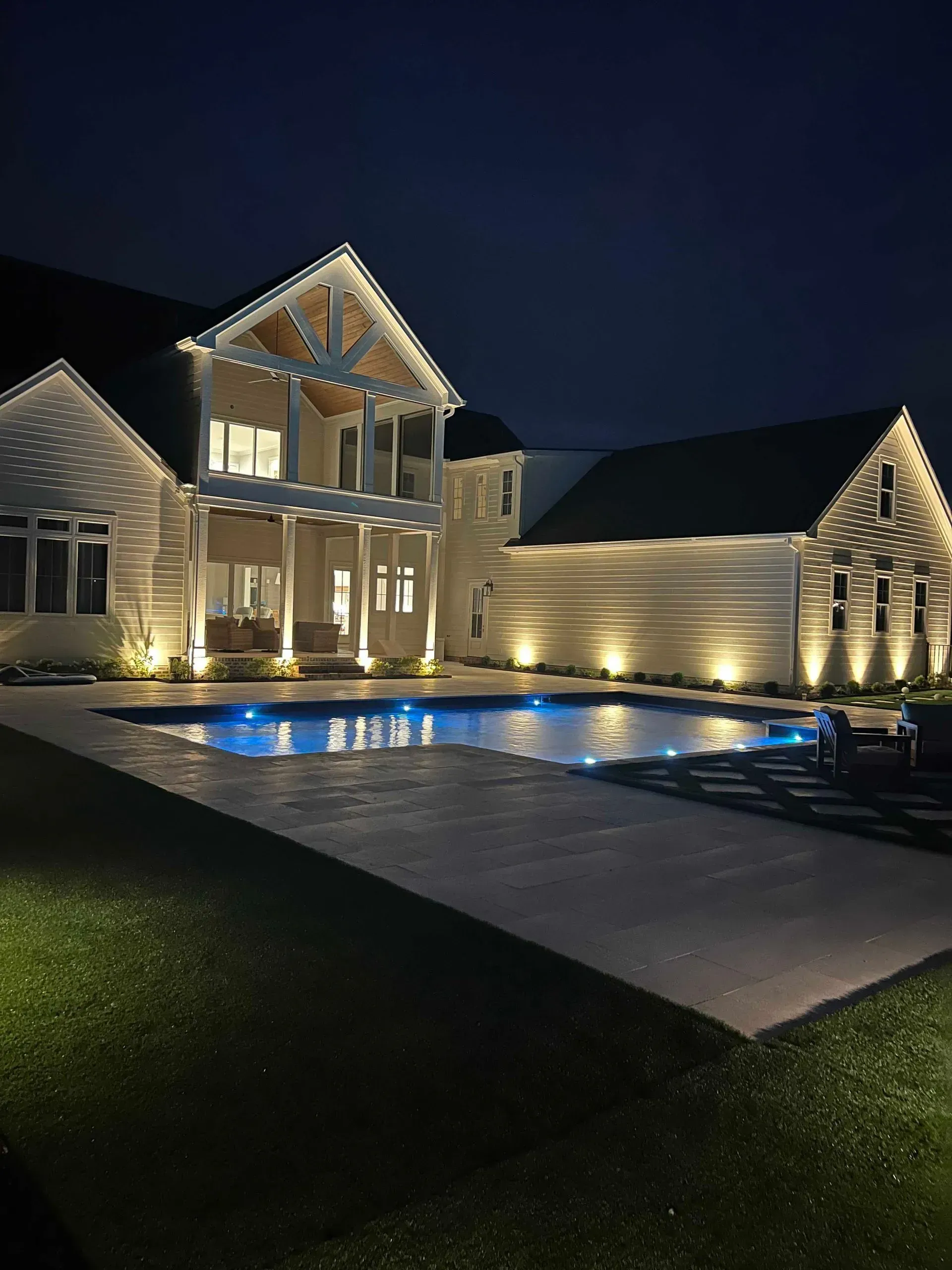 A large house with a swimming pool in front of it at night.