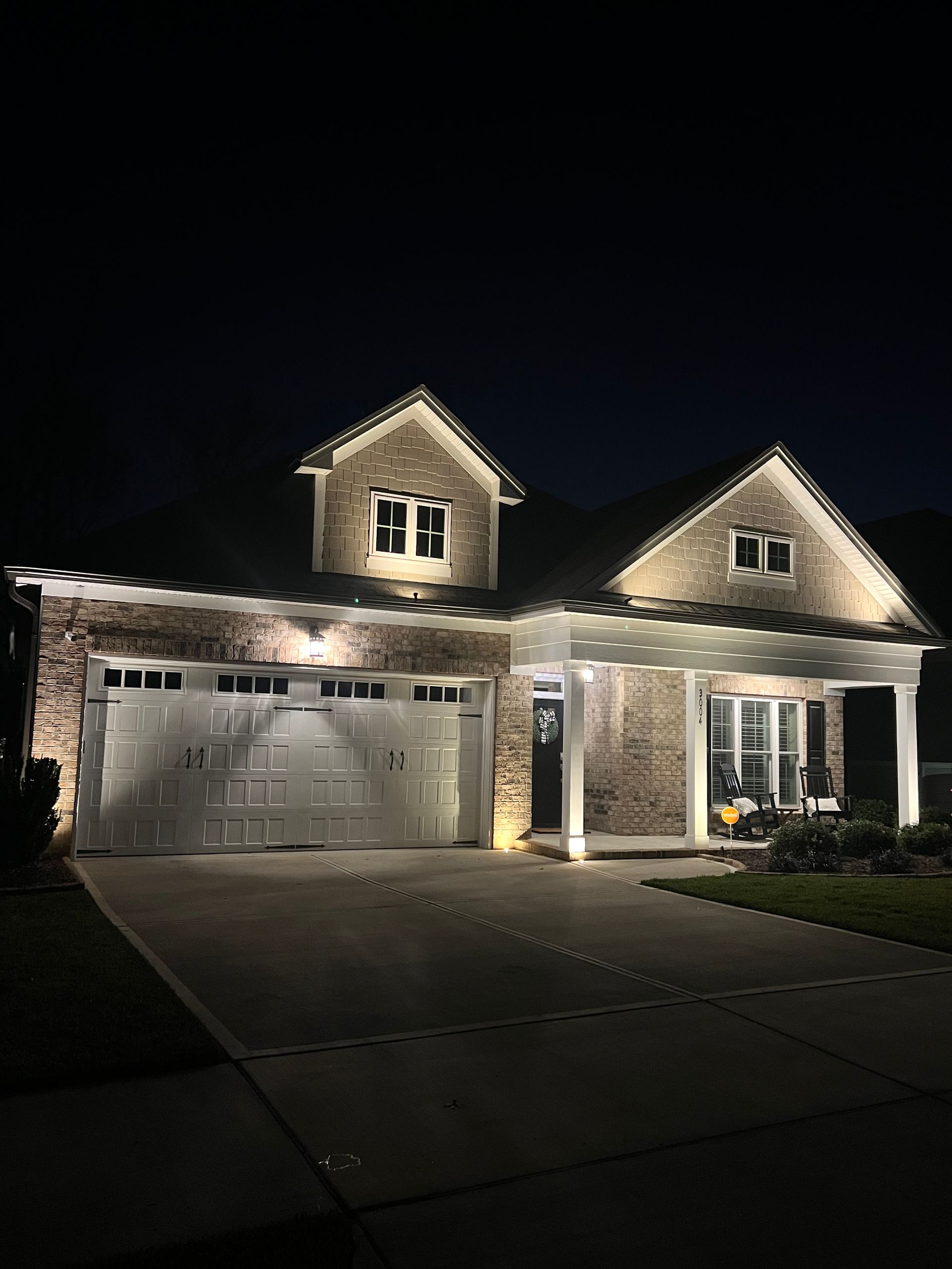 The house is lit up at night and has a large garage.