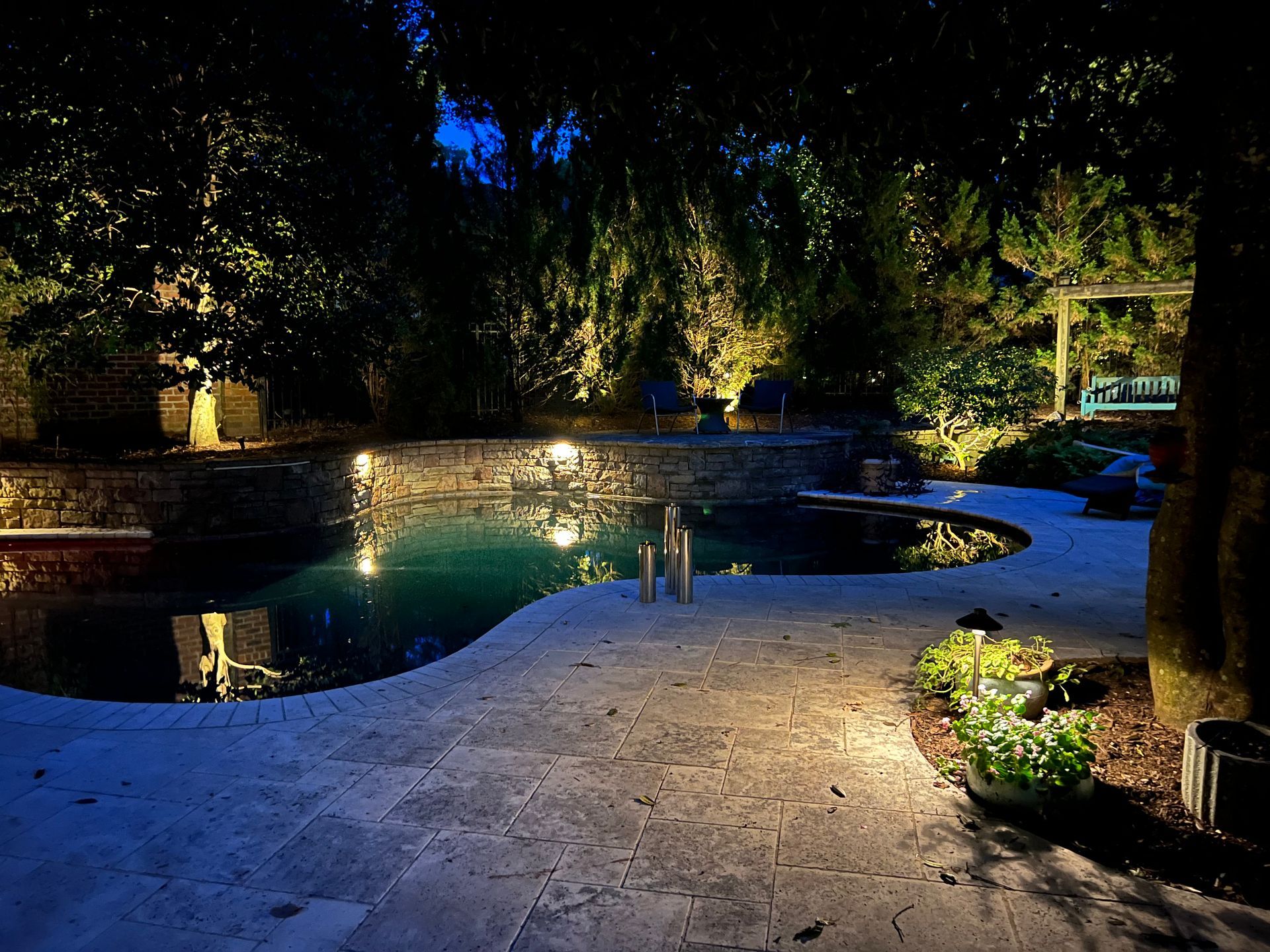A swimming pool is lit up at night in a backyard