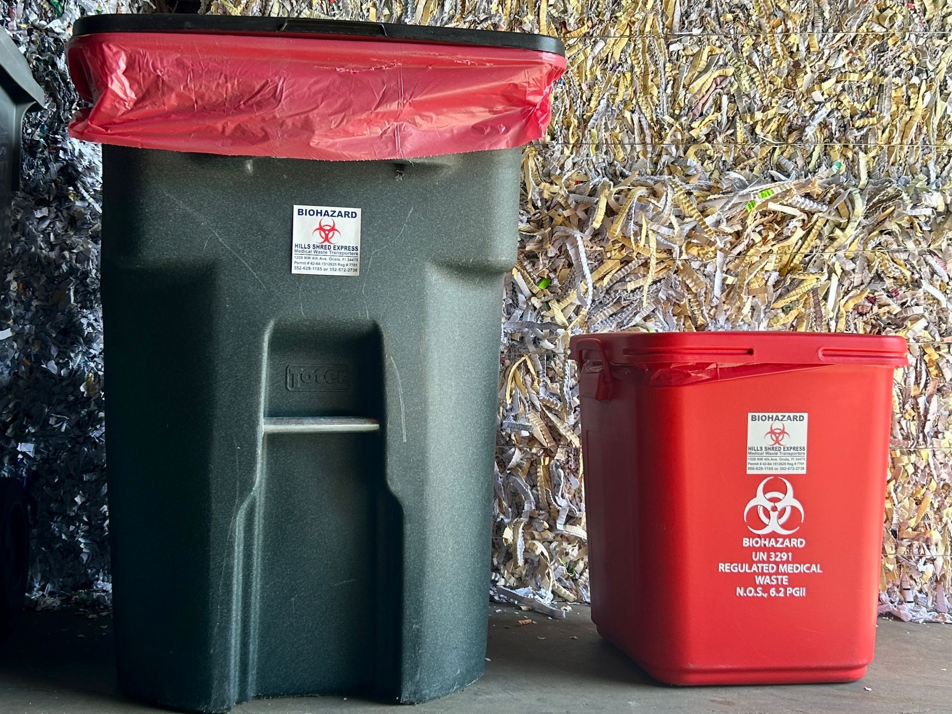 A black garbage can next to a red bin with a biohazard symbol on it