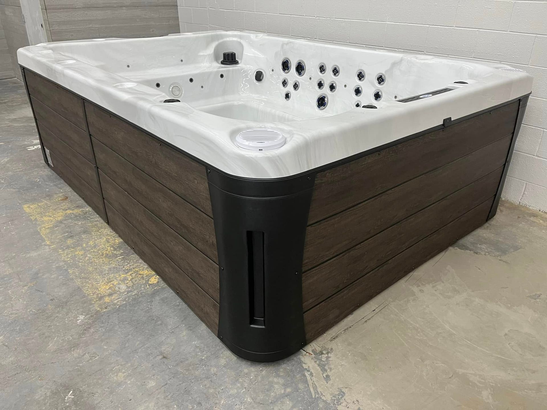 White hot tub with dark wood siding and black corner trim on a concrete floor.