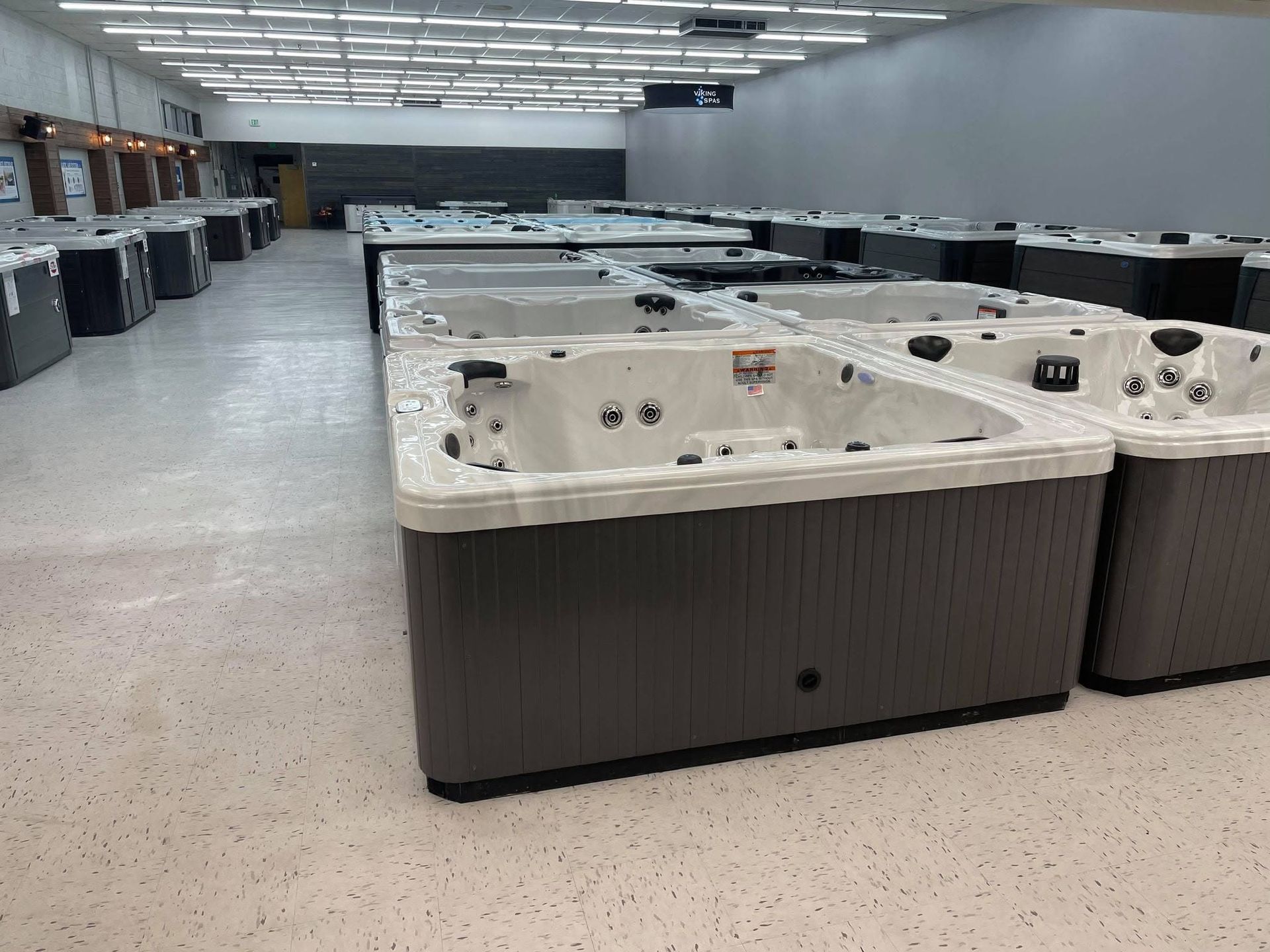 A row of white and brown hot tubs in a showroom under bright ceiling lights.