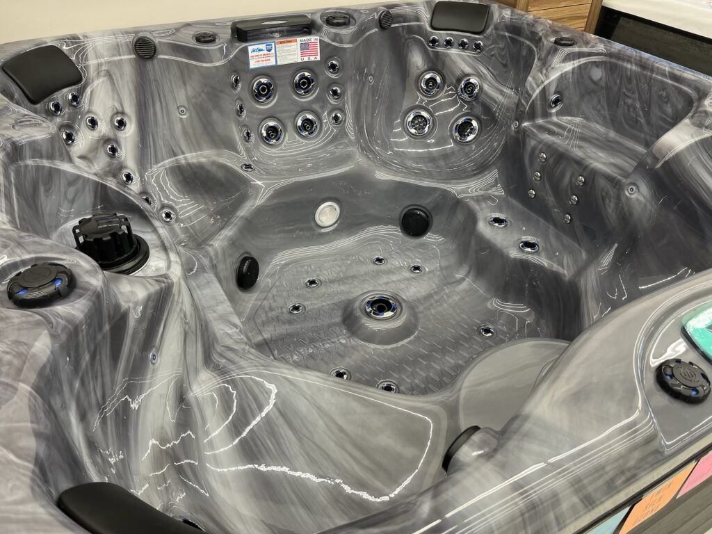 Gray hot tub interior with multiple seats, jets, and control knobs on the side
