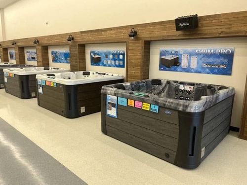 Row of hot tubs in a showroom with beige floors, wood-paneled walls, and blue display signs