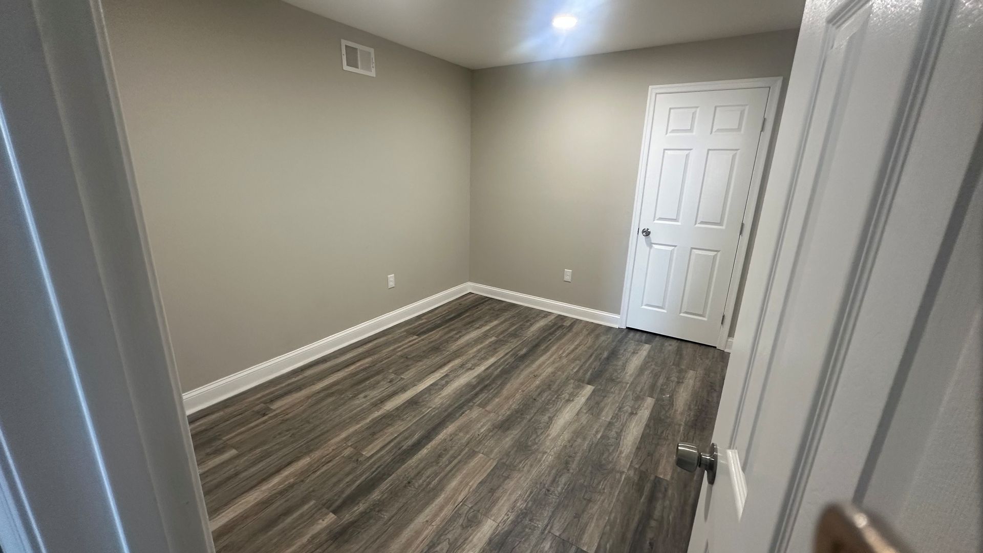 Empty beige room with wood-look flooring and a white door.