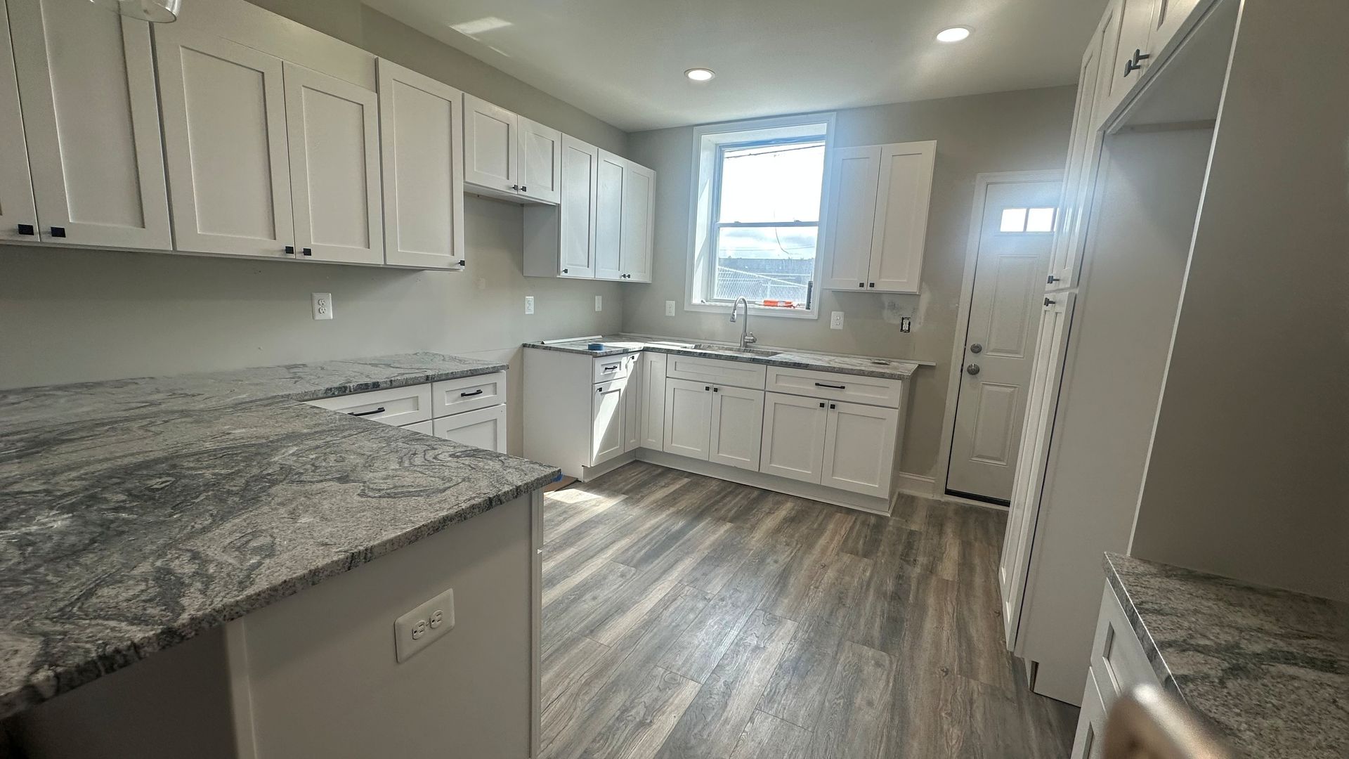 Bright kitchen with white cabinets and wood-look flooring, lit by a window.