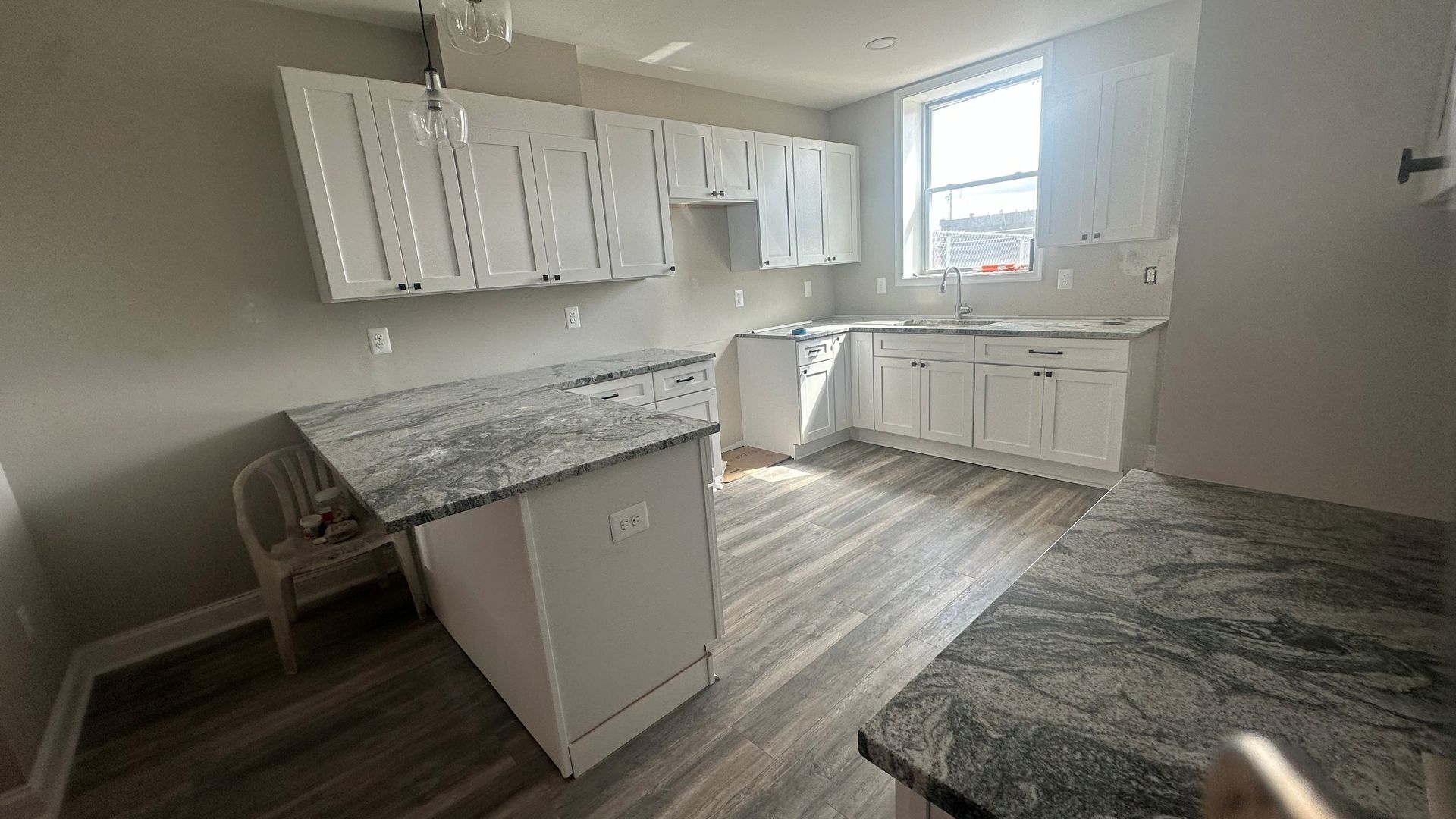 Empty kitchen with white cabinets and a window letting in daylight.