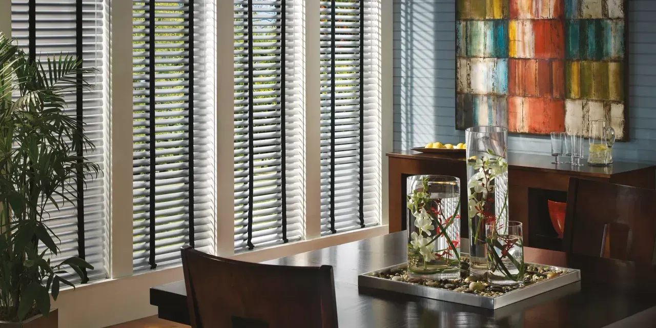 Dining room with a dark wood table, decorative glass vases, and a colorful abstract painting. Windows with blinds are visible.