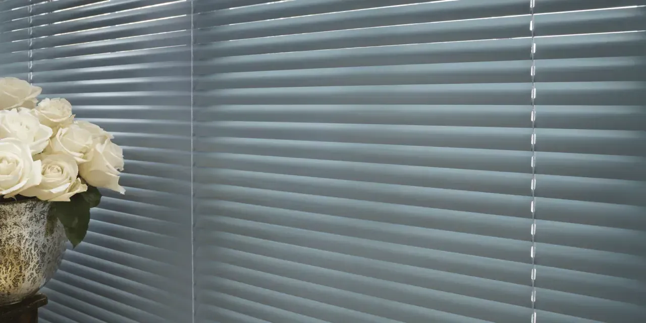 White roses in a textured vase next to closed blue blinds.