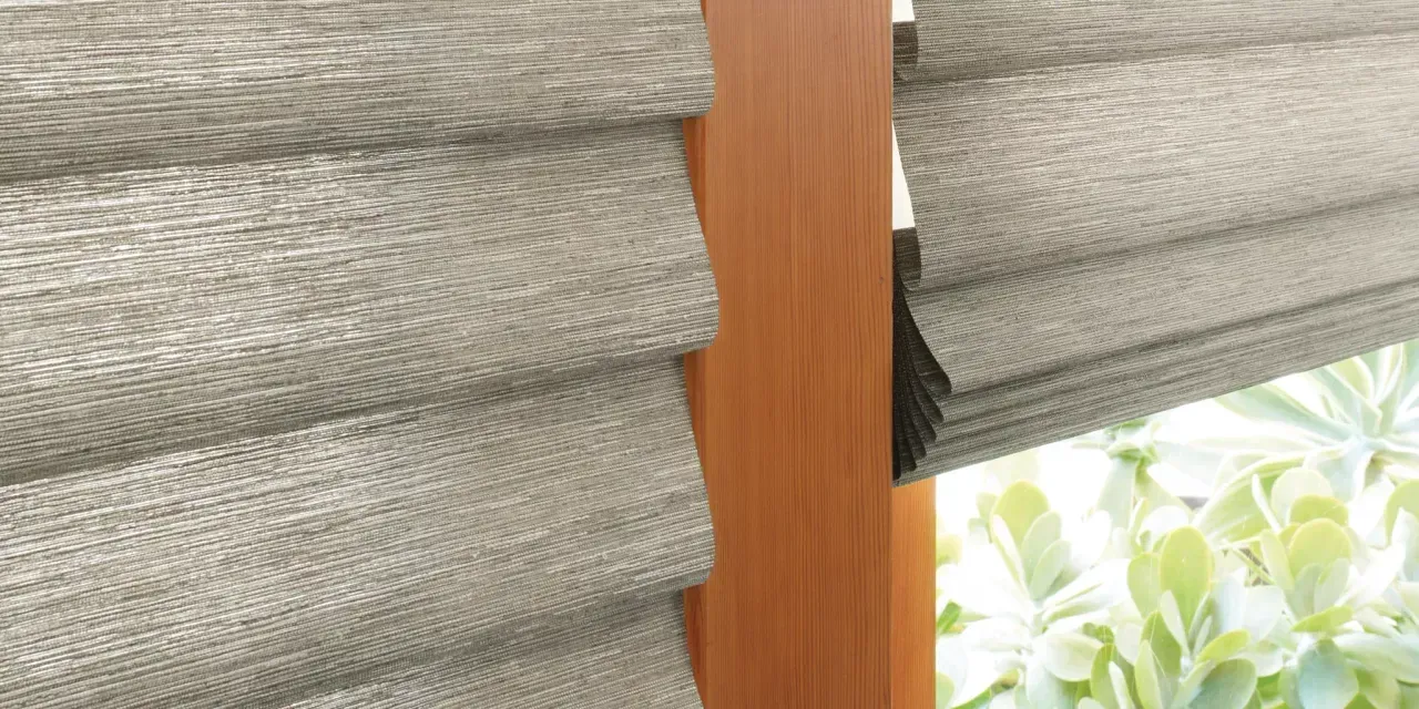 Close-up of textured gray blinds with a wooden beam, likely outdoors with green foliage visible.