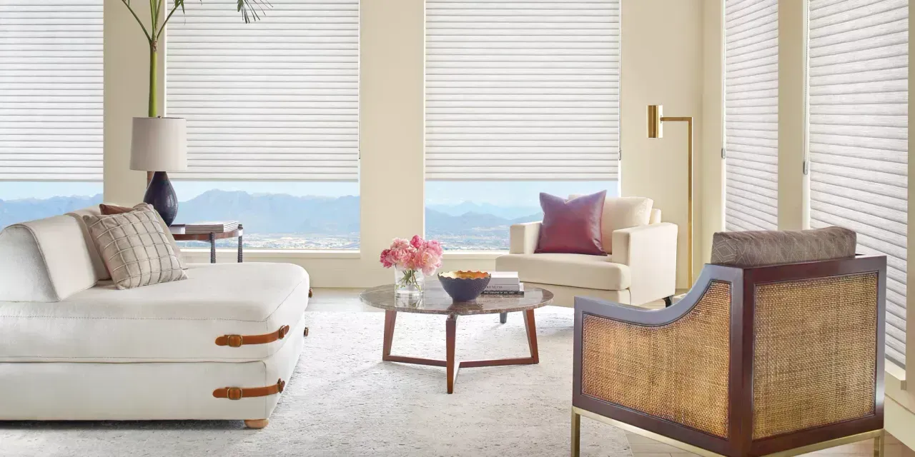 A living room with a white sofa, armchair, and coffee table, with large windows overlooking a mountain range.